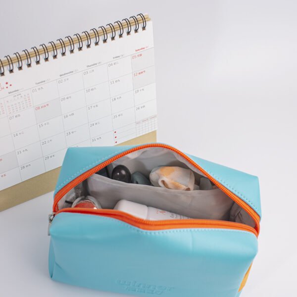Light blue PVC toiletry bag with orange zipper opened Opened custom light blue PVC toiletry bag revealing inner pocket and travel essentials
