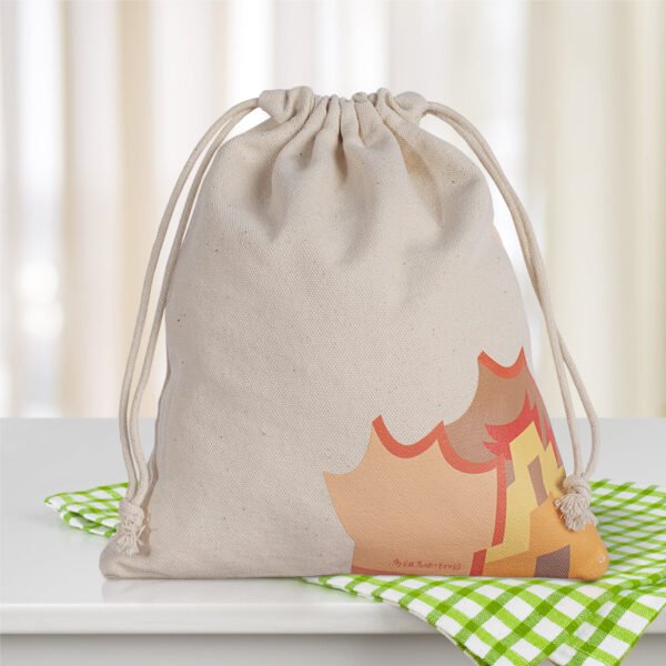 Lifestyle shot of drawstring bag Lifestyle shot of a natural cotton drawstring bag with colorful print placed on a checkered tablecloth.