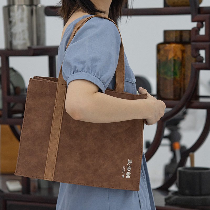Model carrying a custom brown suede PU tote bag with double straps in a traditional tea house setting