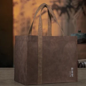 Suede PU tote bag front view Upright brown suede PU tote bag placed on a wooden table with tea accessories background
