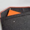 Opened custom felt laptop sleeve showing leather trim, metal snap, and a large inner pocket holding a document.