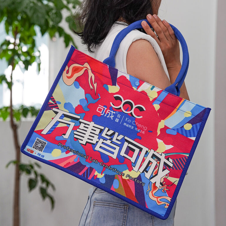 Custom printed canvas tote bag with blue webbing handles and vibrant full-color digital graphics, carried on a model's shoulder.
