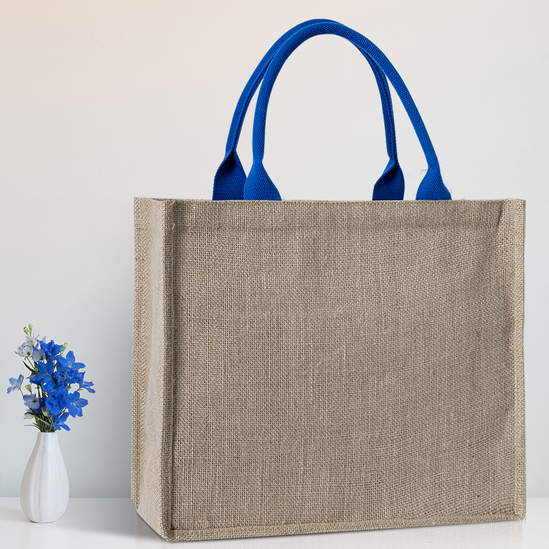 Custom natural jute tote bag with blue woven handles displayed in a minimalist setting.